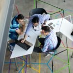Three men collaborating over a laptop in a modern, geometric-themed office space.